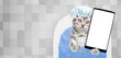 Cute kitten wearing shower cap takes the bath at home and shows big smartphone with white blank screen in it paw. Top down view. Empty space for text