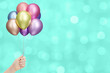 Female hand holds bunch of colorful shiny balloons on blurred aquamarine background. Empty space for text