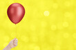 Female hand holding the red balloon on blurred yellow background. Empty space for text