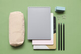 Fototapeta Mapy - Beige pencil case with different school stationery and notebooks on green background