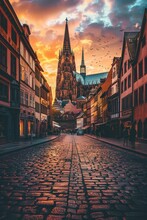 Panoramic View Of A Historic European City, Cobblestone Streets, Quaint Buildings, And A Towering Cathedral Against A Sunset Sky