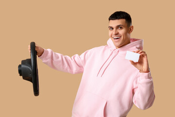 Poster - Young man with steering wheel and blank driving license on brown background