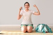 Sporty young woman with inhaler and bag showing muscles near light wall