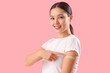 Beautiful young woman pointing at applied medical patch on her arm against pink background