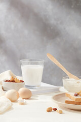 Bowl of flour, eggs and milk bottle featured on wooden chopping board against milk coffee brown background on white kitchen counter. Front view photo with copy space