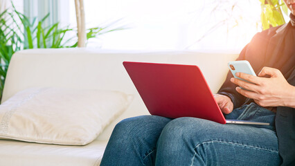 Poster - A man sitting on the sofa and using a smartphone and laptop computer.