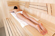 © Nobilior - Woman relaxing in a sauna. She is lying on a towel.