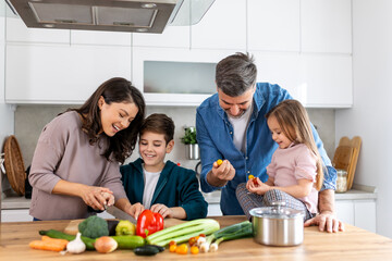 Poster - Happy family cooking together on kitchen. Mother Son and daughter with father cooking. Son and mother chopping green vegetables. Home recreation and food preparation on weekend