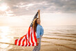 Woman patriot  with american flag on the beach at sunset. USA celebrate 4th of July. Independence Day concept