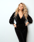 Fototapeta  - Beautiful Blond Hair Woman 40s years old. Fashion Model with Long Curly Hairstyle. Blondie Female in Black Velvet Dress over White