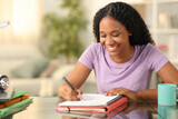 Fototapeta Tematy - Happy black student taking notes at home