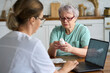 © Westend61 - Senior woman holding medicine bottle with nurse using laptop at home