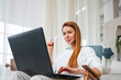 © Westend61 - Woman shopping online through laptop sitting in chair at home