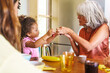 Toddler engages with their grandparent over breakfast- sharing the simple joy of fresh fruit. In a brightly lit kitchen, grandparent interacts with grandchild - wisdom and love across generations.