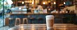 Disposable coffee cup on wooden table in cafe with blurred background.