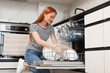 © New Africa - Woman loading dishwasher with plates in kitchen