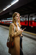 © Big Shot Theory - Female standing at subway platform with mobile phone, using social media and waiting train