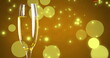 Image of confetti falling over glass of champagne on yellow background