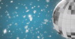 Image of mirror disco ball spinning over snow falling on blue background