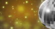Image of mirror disco ball spinning over spots of lights on yellow background