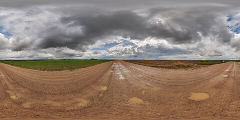 Wall Mural - hdri 360 panorama on wet gravel road with puddles among fields in spring nasty day with storm clouds in equirectangular full seamless spherical projection, for VR AR virtual reality content