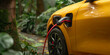 Yellow electric plug-in car charging. Green plants on background. Eco energy concept.