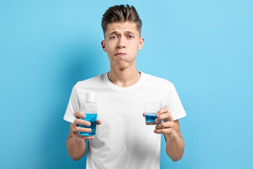 Canvas Print - Young man using mouthwash on light blue background