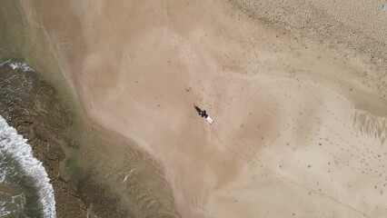 Wall Mural - Drone shot over a couple relaxing on sandy beach by seawater with sunlight