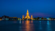 Wat Arun stupa, a significant landmark of Bangkok, Thailand, stands prominently along the Chao Phraya River, with a beautiful night sky.