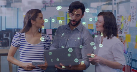 Poster - Globe of digital icons against diverse male and female office colleagues using laptop at office