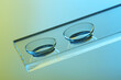 Pair of contact lenses on glass against color background, closeup