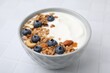 Bowl with yogurt, blueberries and granola on white tiled table, closeup