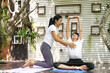 Training women yoga instructor helping student to master position exercise in private class in nature garden home.Â  Healthy and sport activity Concept