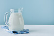 Milk in jug and glass on wooden table and blue background. Concept of farm dairy products, milk day. Kitchen or supermarket mock up for design. Copy space.