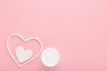 Wall Mural - White heart shapes with cream jar on light pink table background. Pastel color. Care about female face, hands, legs and body skin. Closeup. Empty place for text. Top down view.