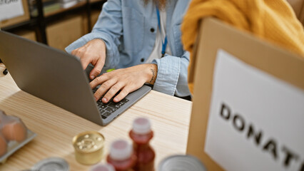 Sticker - Man's hands at work, a dedicated volunteer sitting at a table, engrossed in charity work on his laptop in community center, surrounded by donation boxes.