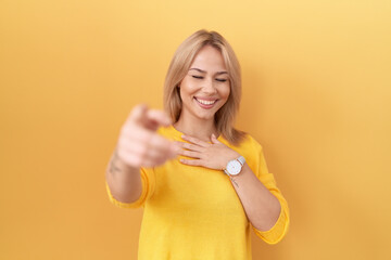 Sticker - Young caucasian woman wearing yellow sweater laughing at you, pointing finger to the camera with hand over body, shame expression