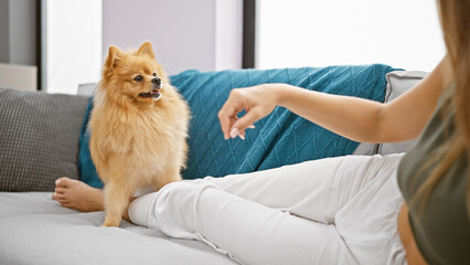 Sticker - Heartwarming indoor portrait of a young hispanic woman playfully bonding with her lovable dog, lying on a sofa in her cozy living room at home, radiating happiness and touch of affection.