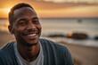 Authentisches Porträt eines Afroamerikaners mit strahlendem Lächeln im warmen Sonnenuntergangslicht am Meer