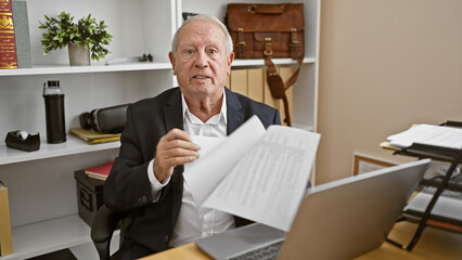 Canvas Print - Serious, mature gentleman hard at work, elegant white-haired senior man, a seasoned business professional, engrossed in documents while speaking earnestly at the office.