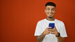 © Krakenimages.com - Cheerful young latino man engrossed in online texting on his trendy smartphone, with a vibrant isolated red backdrop illuminating his handsome happiness