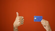 © Krakenimages.com - Man's tattooed hands thrust a credit card over isolated red background with an a-okay gesture - thumbs up in approval
