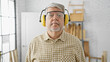 Mature man with grey hair wearing safety earphones and glasses in a workshop.