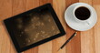 Image of tablet with light trails on screen and cup of coffee on desk