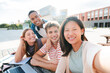© Jose Calsina - A group of happy and diverse teenagers smiling, taking a selfie portrait together during a student gathering. Young friends of various ethnic backgrounds laugh and capture the moment with a smartphone