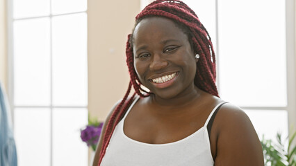 Canvas Print - Smiling african american woman with red braids posing in a bright living room.