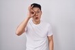 Young asian man standing over white background doing ok gesture shocked with surprised face, eye looking through fingers. unbelieving expression.