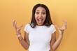 © Krakenimages.com - Young arab woman wearing casual white t shirt over yellow background crazy and mad shouting and yelling with aggressive expression and arms raised. frustration concept.