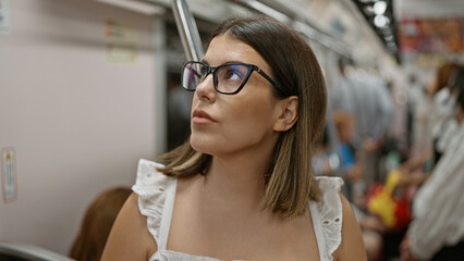 Sticker - Beautiful hispanic woman with glasses standing, waiting amidst subway transit, urban city's portrait of a modern brunette passenger inside empty underground railway, travel in public transport