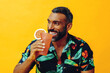 handsome bearded mid adult african american man smiling on vacation sitting on a chair drinking orange juice cocktail